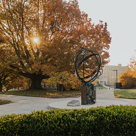 the sundial on a bright fall day with beautiful fall trees behind it