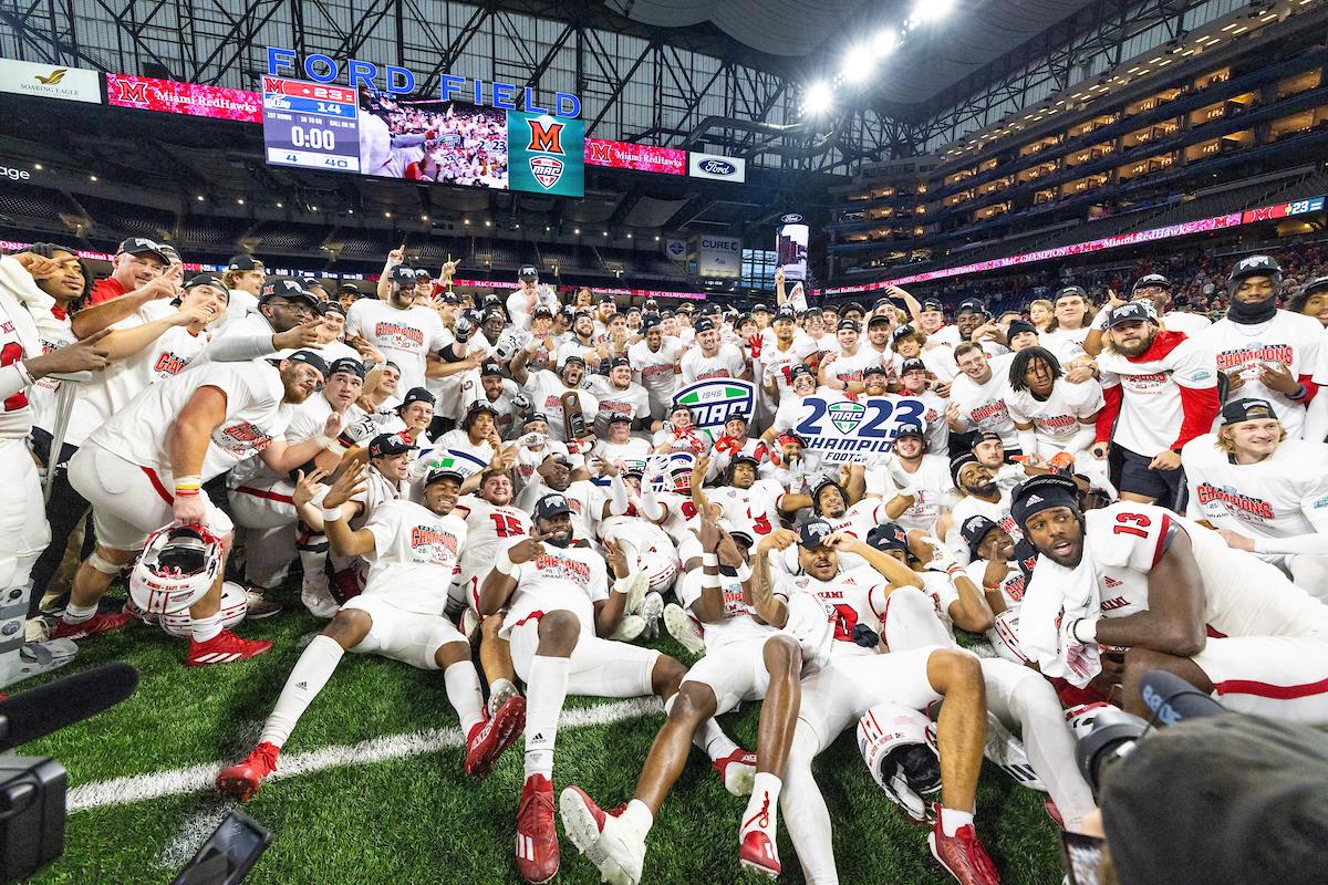 The Miami University football team huddles together holding the 2023 MAC championship trophy in triumph