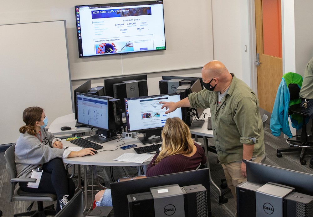 High school students participating in the bridges program writing at desks while a Miami professor looks on