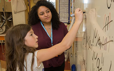 A student teacher helping a student write on a whiteboard.