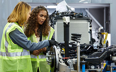 2 females wearing yellow vests working on a piece of equipment.