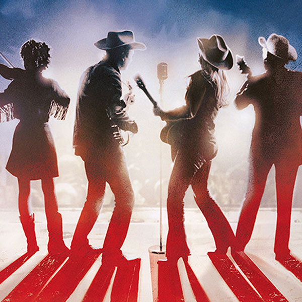 4 figures standing on a stage with an American flag in the background.