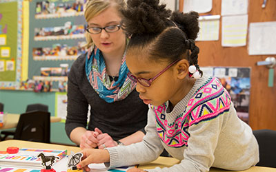 A pre-kindergarten teacher working with a student at a table.
