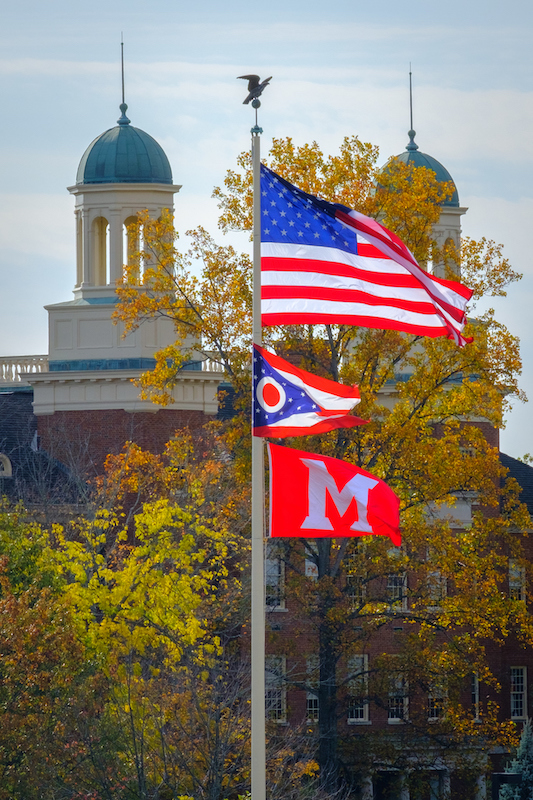 Harison Hall in the background with the America flag, Ohio flag, and Miami flag on a pole.