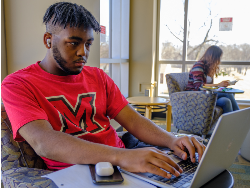 一名学生在图书馆边听音乐边用笔记本工作。