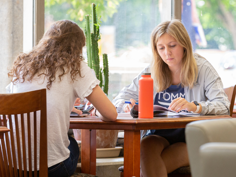 Dos estudiantes sentadas en una mesa trabajando en un proyecto grupal.