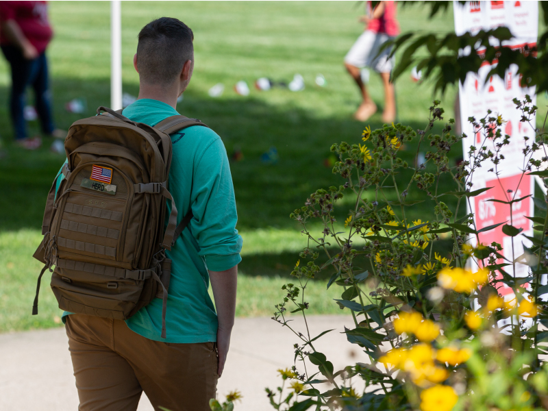 Un estudiante caminando en el exterior con una mochila que tiene la bandera de EE. UU.