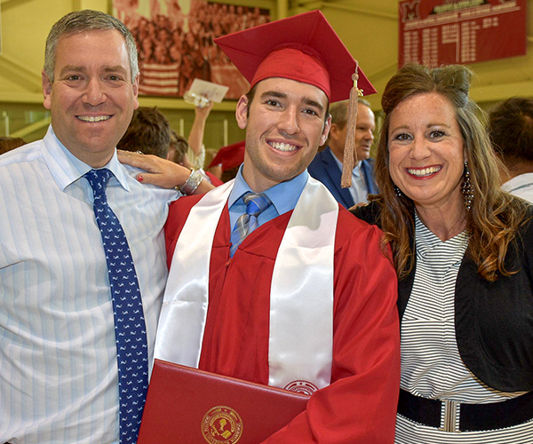 Un estudiante graduado con toga y birrete sosteniendo su diploma y sonriendo junto con sus padres.