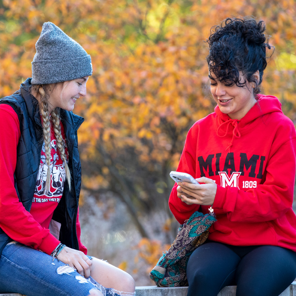 2 students sitting outside looking at a phone