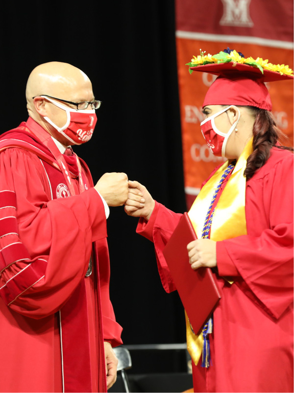A graduate fist bumping with President Crawford after receiving her diploma at graduation.