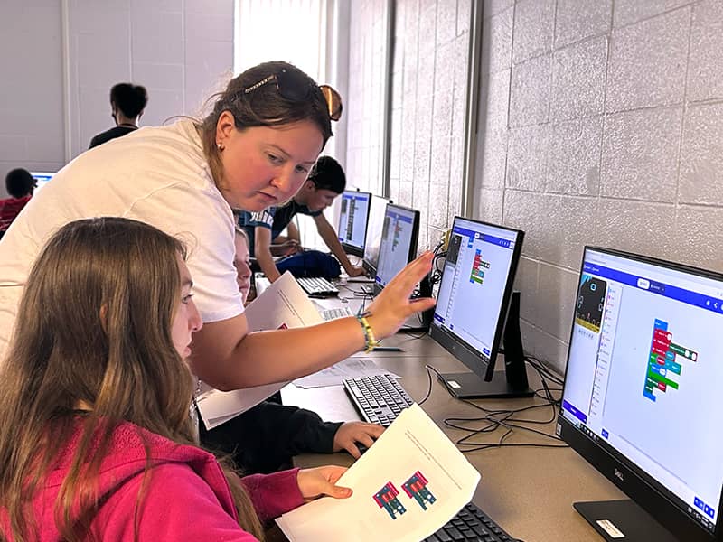 A STEAM counselor helping a camper with writing programming code