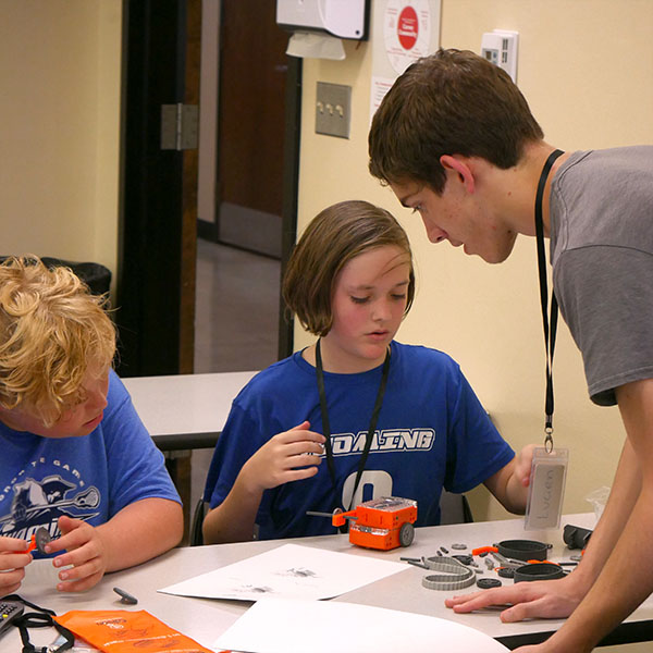 Leader in training helping campers assemble robots