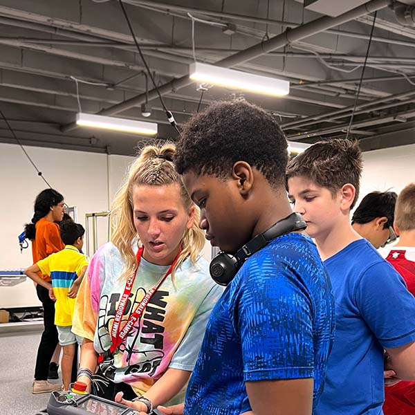 STEAM counselor assisting a camper with a robotics arm