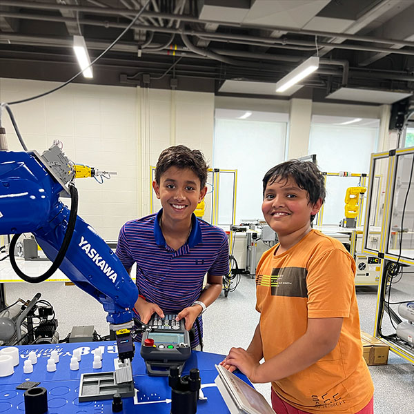 Two campers learning how to operate a robotic arm