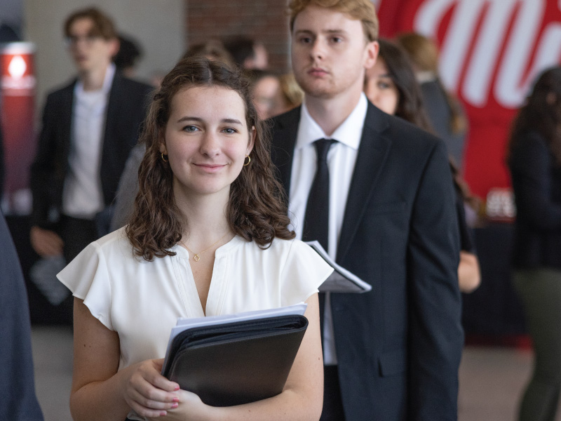 A student smiling holding a black pad-folio. 
