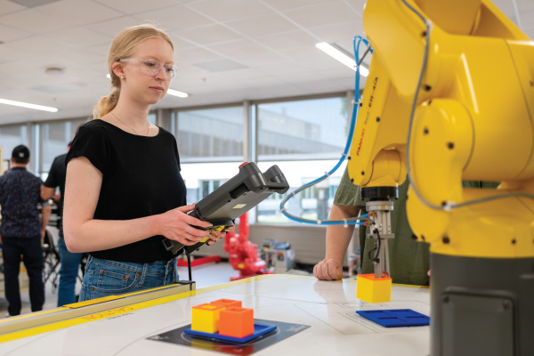 A student working the controller for a yellow robotics arm