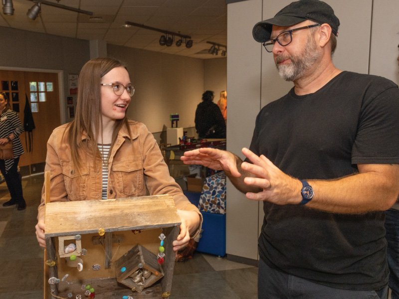 A student talking with her professor about the art project she is holding.