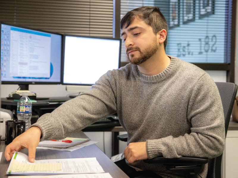 Professional studies student looking at a piece of paper and a computer in the background. 