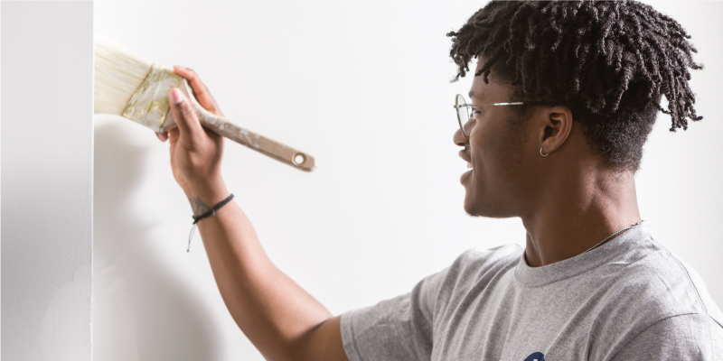 A Service+ student painting the interior walls of a house with a paint brush.