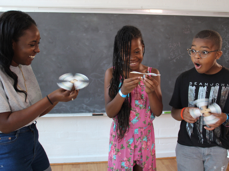 Americorp change agent showing 2 kids how to use a homemade pin wheel. 