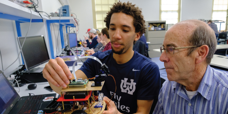 A young man shows a professor a robotic vehicle he created in a Miami Regionals lab.