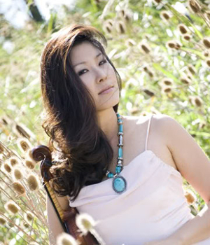 Cecilia Suhr standing in a field of tall grass with her violin.