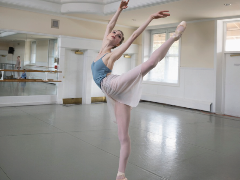 Claire Barrington in her ballet outfit standing on her tiptoes of one foot and the other kicked behind her with her arms above her head.