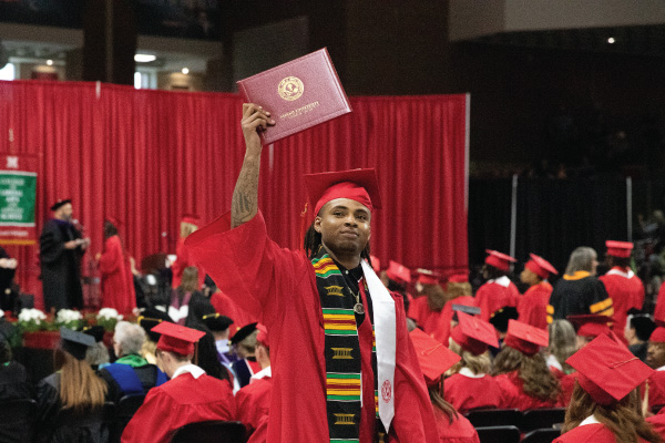 2024 CLAAS graduate holding up her diploma at commencement in his cap and gown.