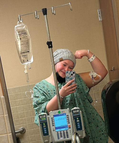 Holly Thornton in the hospital bathroom with an iv in her arm holding it up in a mirror in a strong position.