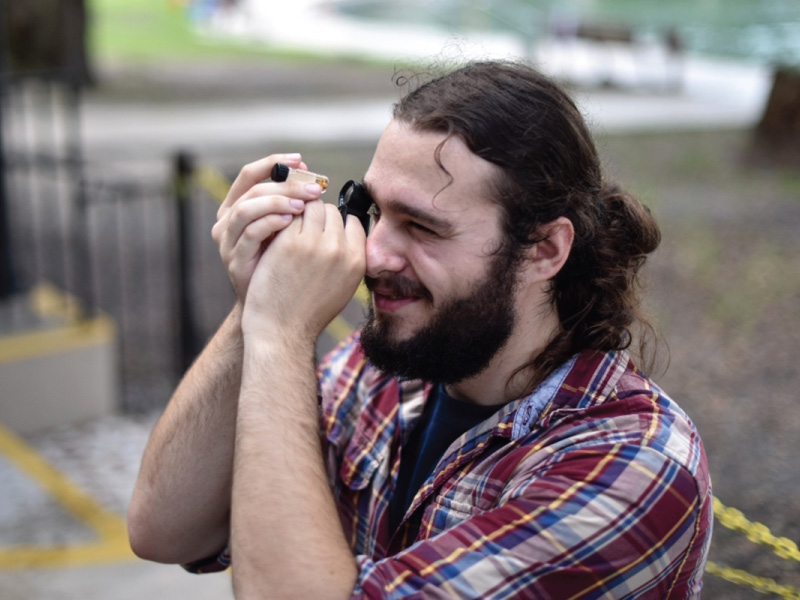 Andrew Cannizzaro looking thru a magnifying glass at a small glass bottle.