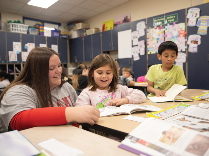Hazel Moon working with 2 students in the classroom at a table.