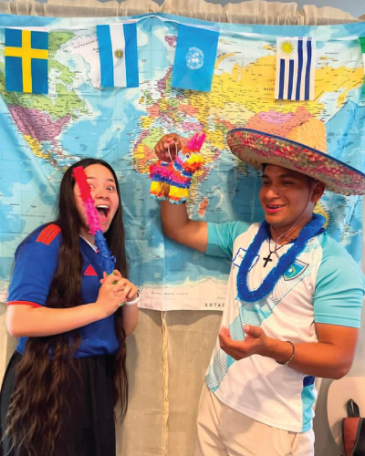 Martin Raymundo and a friend posing in front of a map and different flags with a sombrero and piñata.