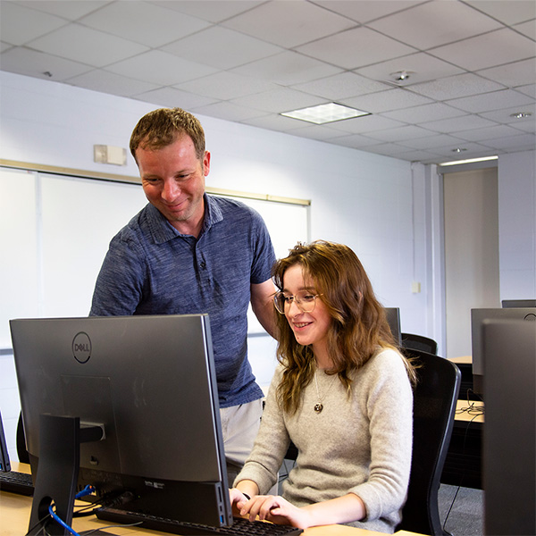 A system support specialist working on a computer with her colleague watching