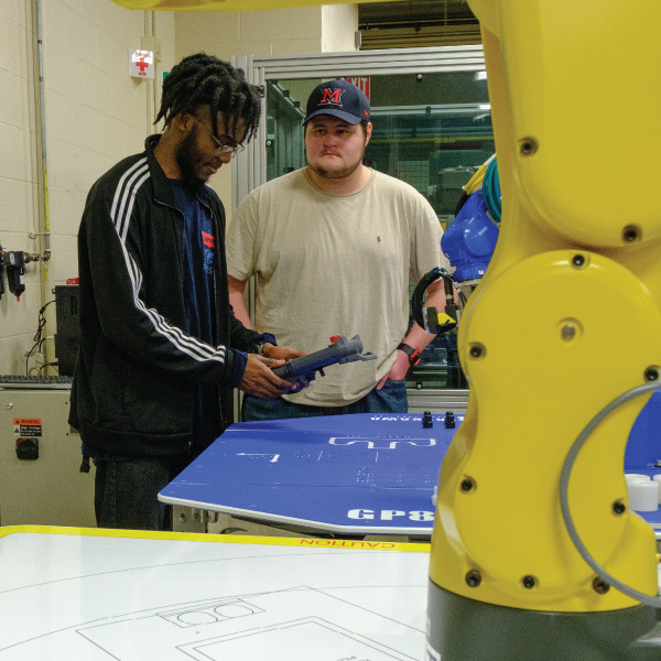 2 students using a remote to control a robot arm. 