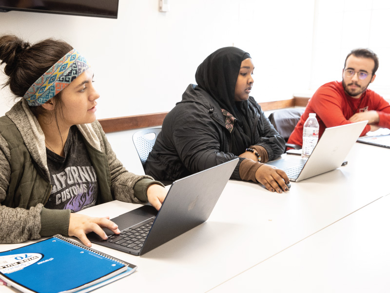 3 students sitting at a table working on a project together.