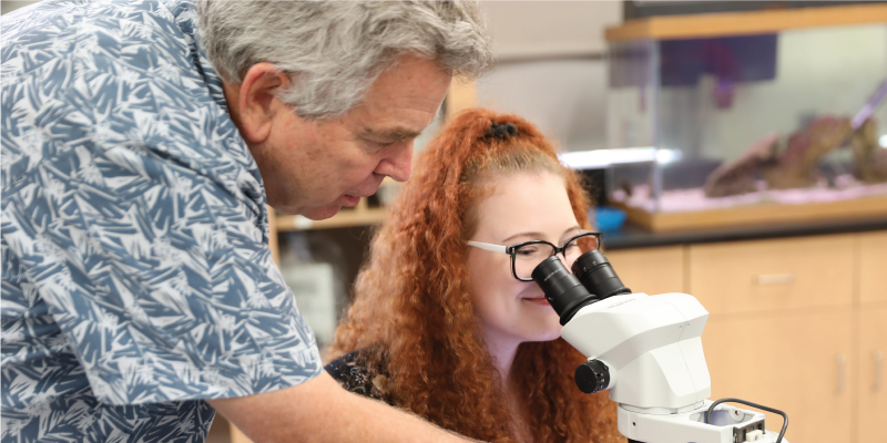 A professor helping a student use a microscope