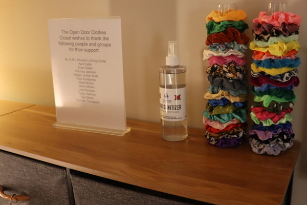 Surface in the closet with two stands filled with scrunchies. Hand sanitizer and a thank you sign are also on the surface.