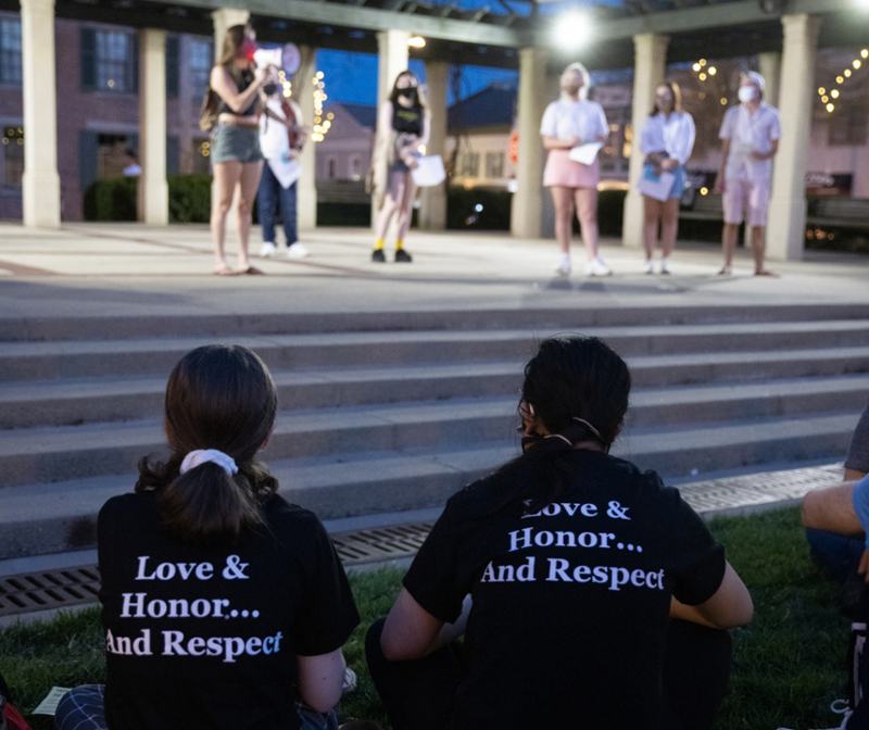 Take back the night rally, with a group of students on the stage in uptown parks and students where love and honor and respect tshirts in the audience.