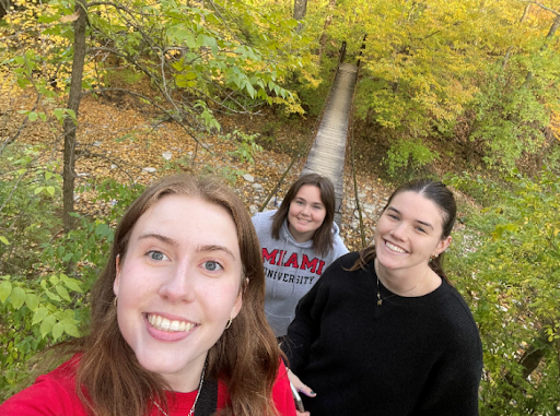 A group of three Miami students walking across a wooden bridge in the woods.