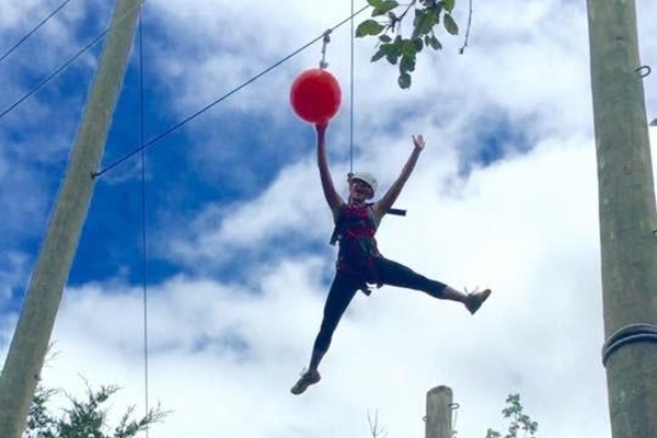 Student on high ropes challenge, hanging from a line high in the air.