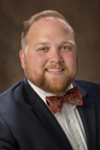 Jonathan James is white man with short dark blonde hair and beard. He is wearing a navy blazer and a snazzy red bowtie with a paisley pattern.