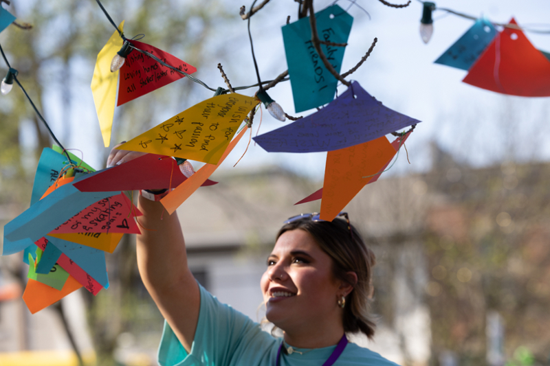 Student reaching up to a tree, which have multi-colored papers with messages written on them.