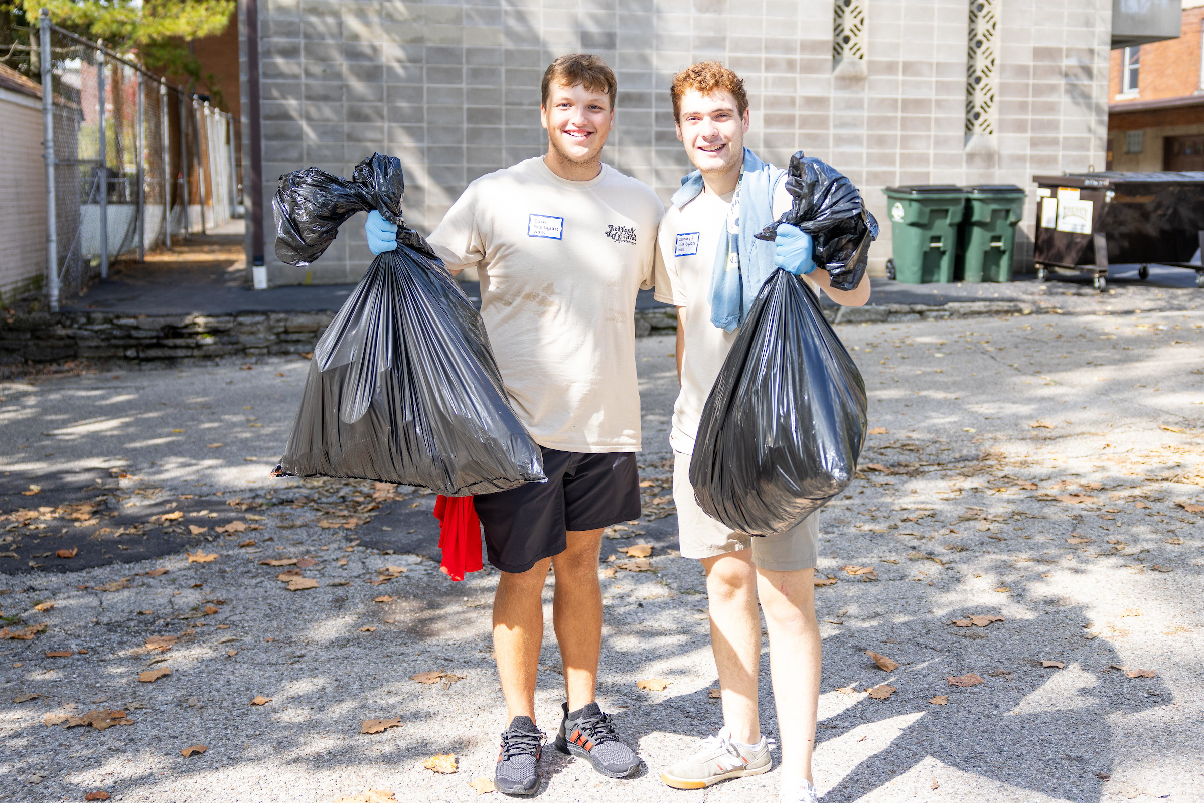 Two students hold up bags of trash uptown