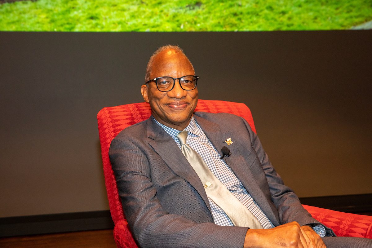 Wil Haygood is seated in a red chair in front of a projection screen