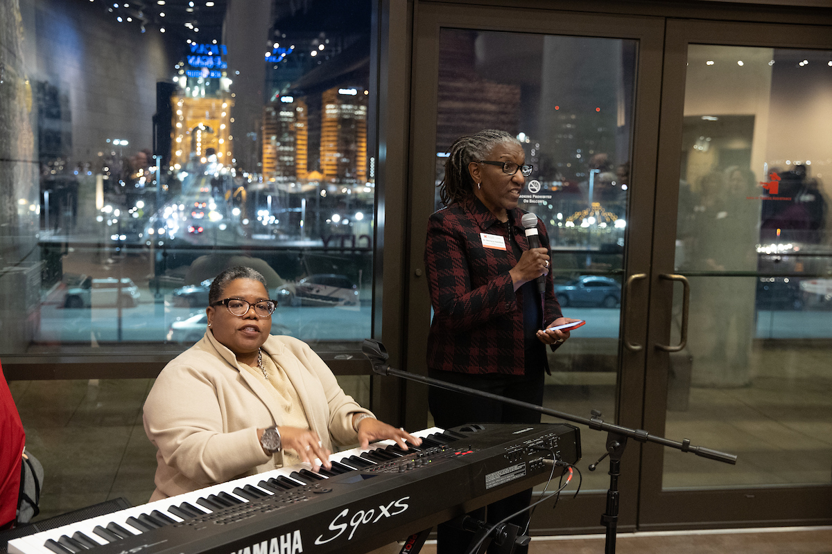 Tammy Kernodle sits at a keyboard playing while Bennyce Hamilton stands beside her singing into a microphone. 