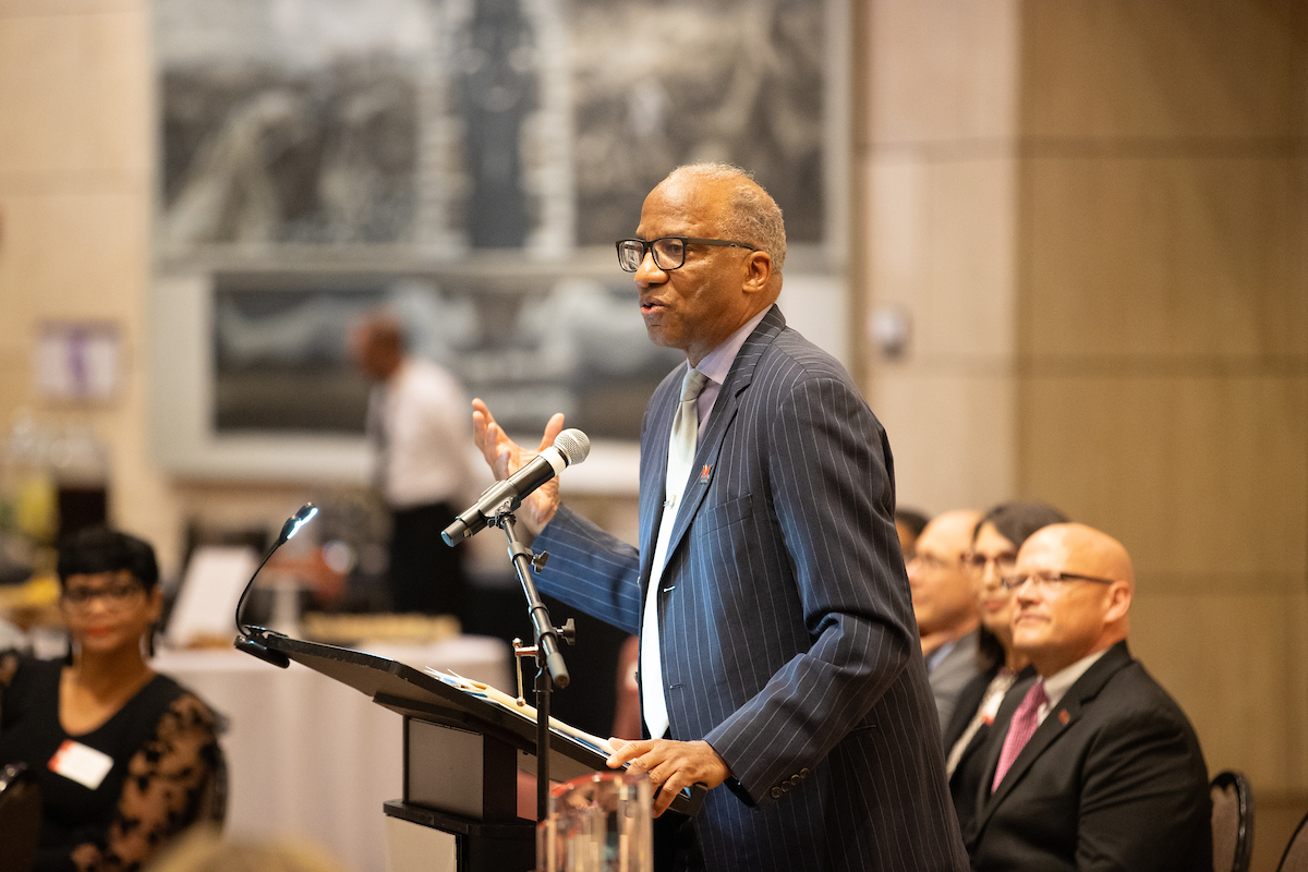 Wil Haygood stands at a podium, speaking into a microphone with his hand raised.