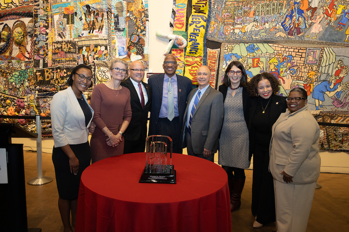 Pictured left to right are Jules Jefferson, Dr. Renate Crawford, President Greg Crawford, Wil Haygood, Chris Makaroff, Cristina Alcalde, Nyah Smith, and Tammy Kernodle. The group stands behind a table with the FS64 award on display.