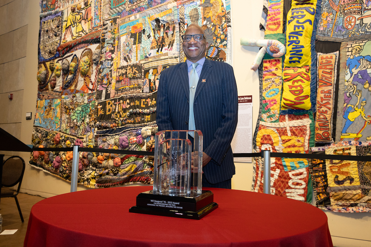 Wil Haygood stands smiling at the camera behind the FS64 award, placed on a table.