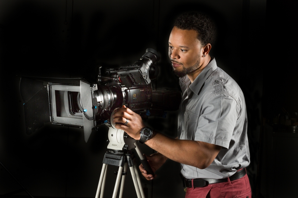 Portrait of Omari using a video camera on black background