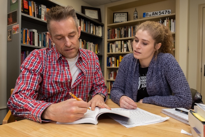 A student works closely with a faculty member reviewing a text book in the library